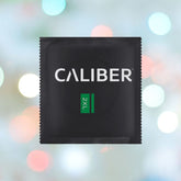 A black "Caliber 2XL - Extra Large Condoms (64mm Wide)" package featuring "2XL" in a green rectangle, set against a blurred background of multicolored circular bokeh lights.